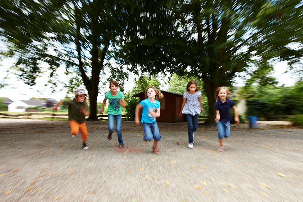 Fünf Jungen und Mädchen rennen in einer Reihe über einen Platz.