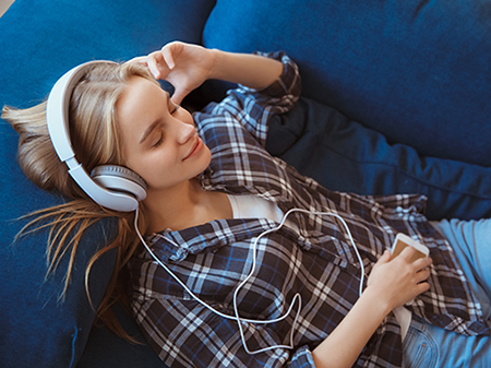 Ein Mädchen liegt mit geschlossenen Augen auf einem Sofa und trägt Kopfhörer.